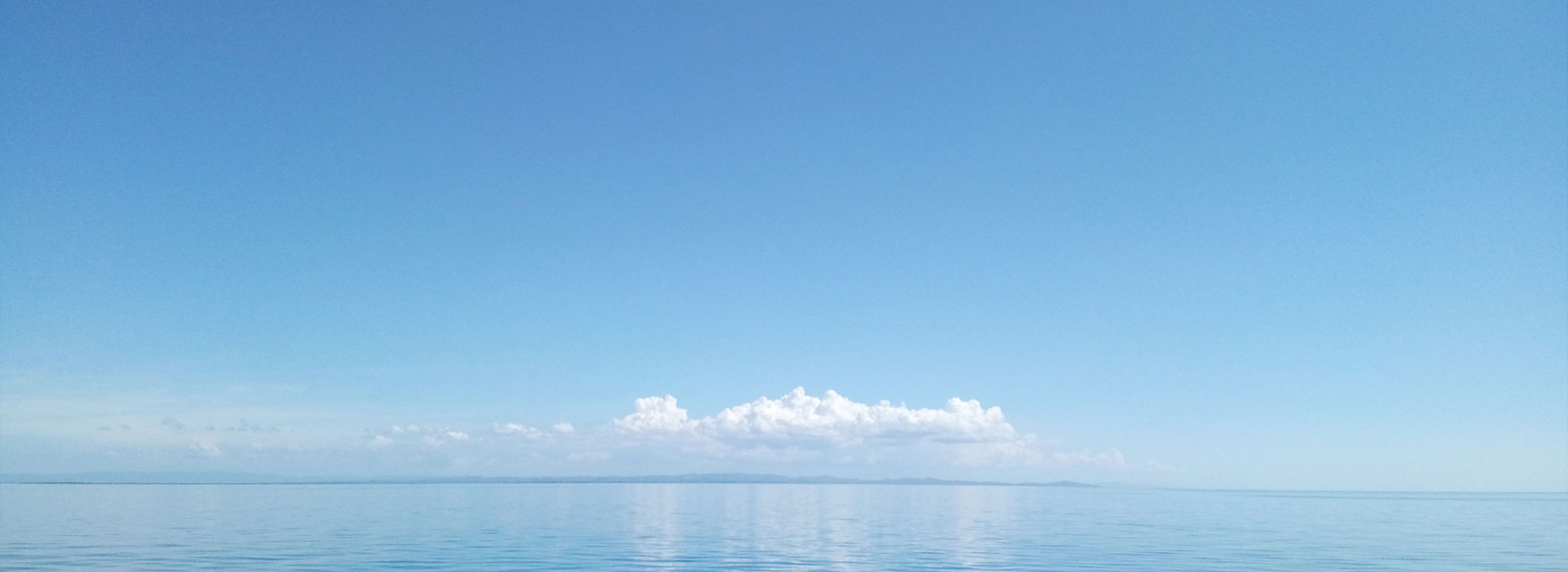 A calm blue ocean meets a clear blue sky with a thin band of clouds.